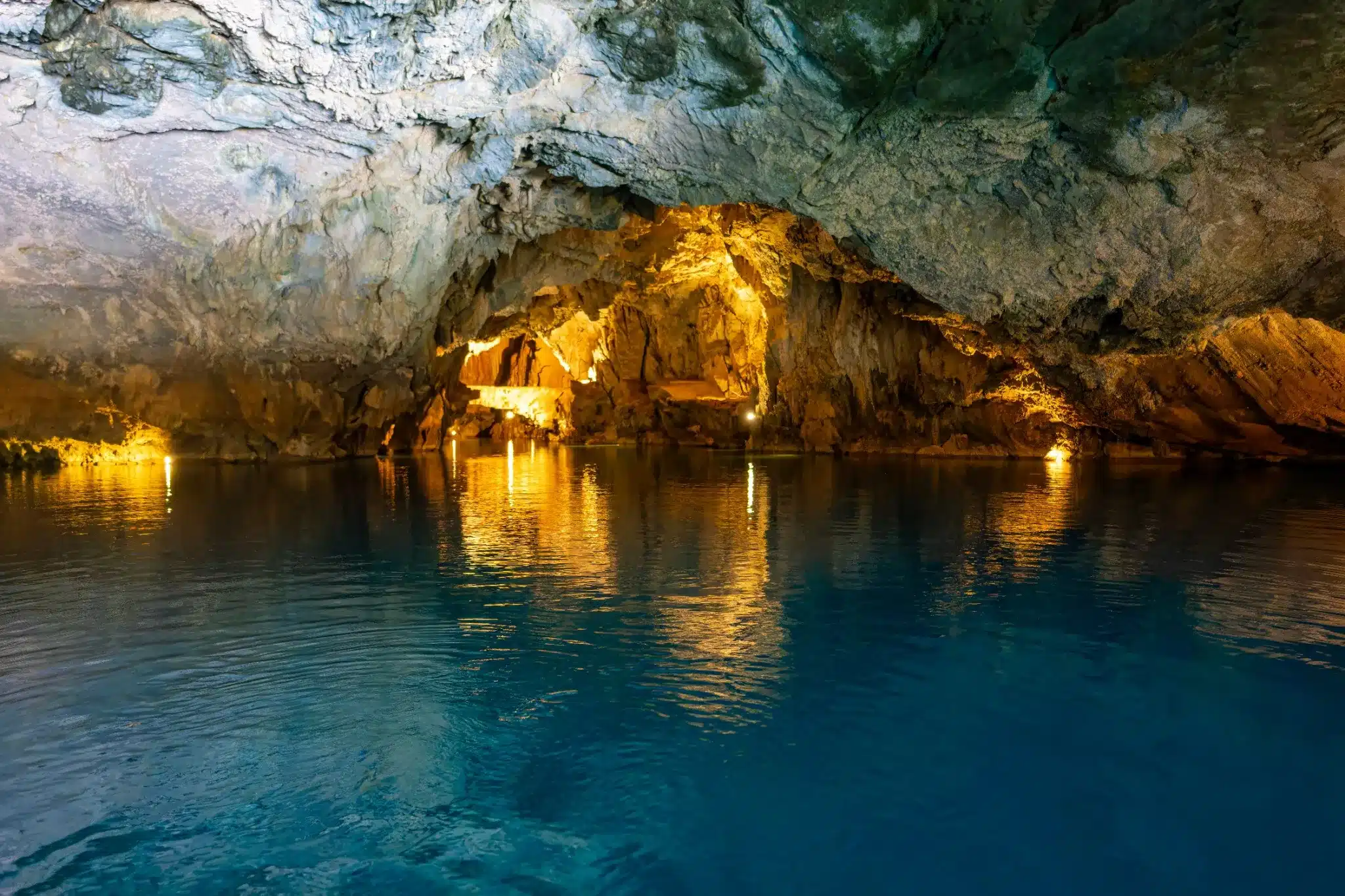 Binnenkant van de Altınbeşik-grot in Antalya, Turkije met helderblauw ondergronds meer en warme verlichting die de rotsen goudkleurig laat oplichten.